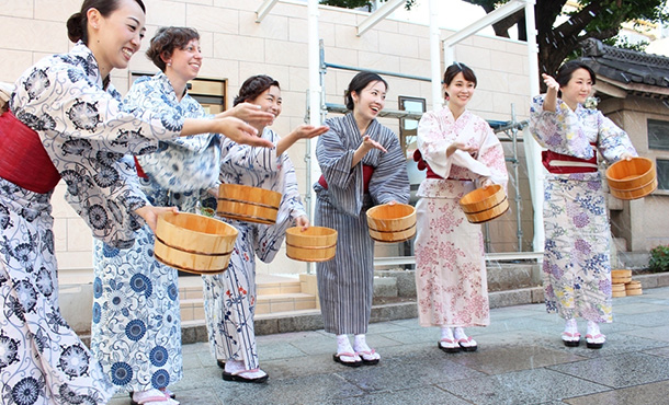 People wearing yukata splashing water on road.